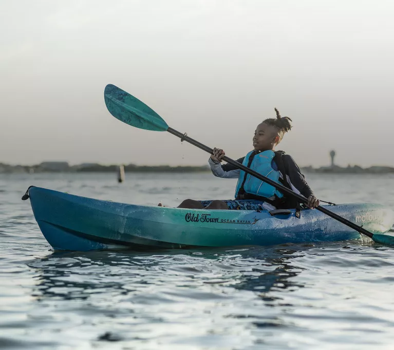 A young boy paddles a blue Ocean Kayak. 