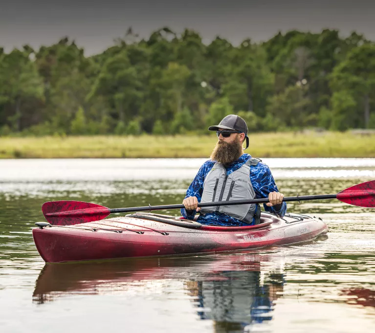 A bearded man paddles a red Old Town Loon kayak.