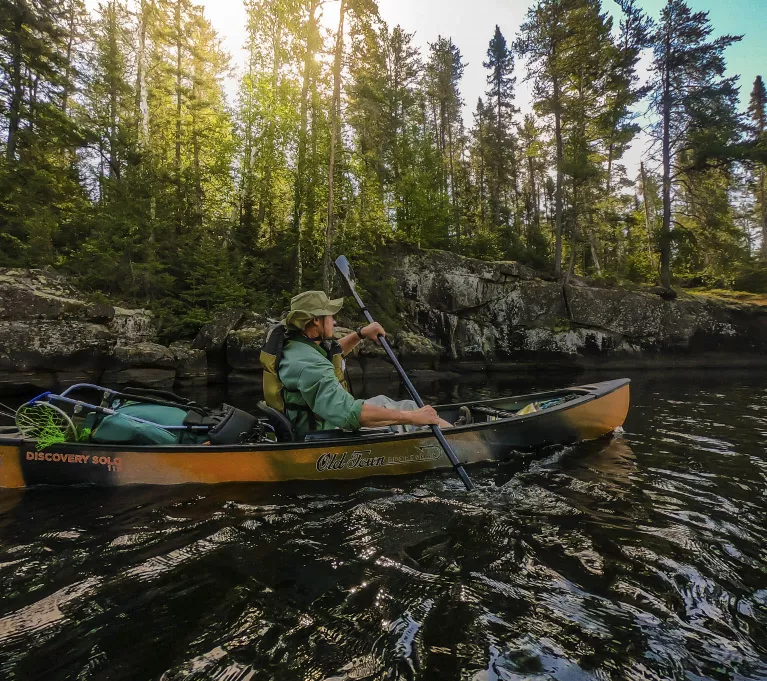 A man paddles an orange solo canoe on a river.