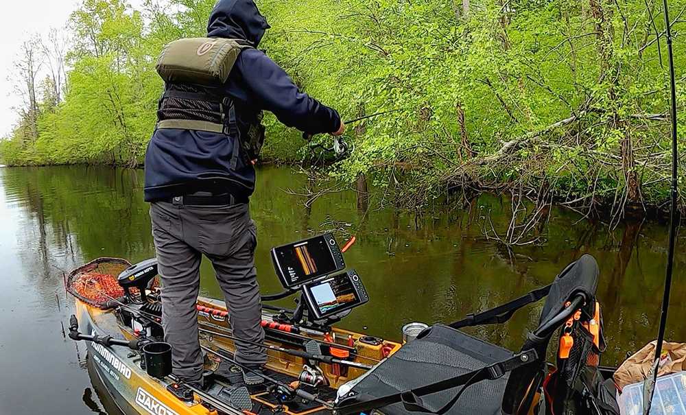 A male kayak angler stands and flips a soft plastic lure towards a largemouth bass spawning bed while on his AutoPilot 136 kayak. 