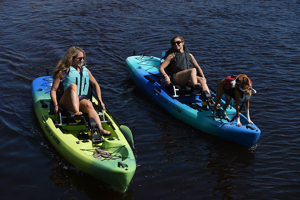 Two girls in Ocean Kayak Malibu Pedal kayak pedaling out on water with their dog