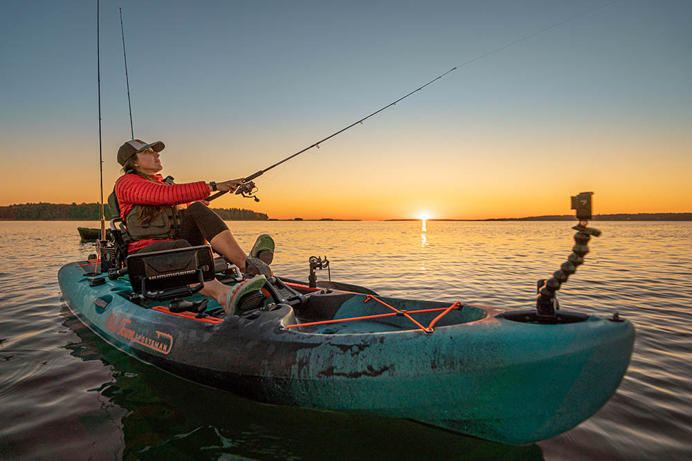 Woman fishing from Old Town Sportsman 120 PDL fishing kayak with sunsetting in distance