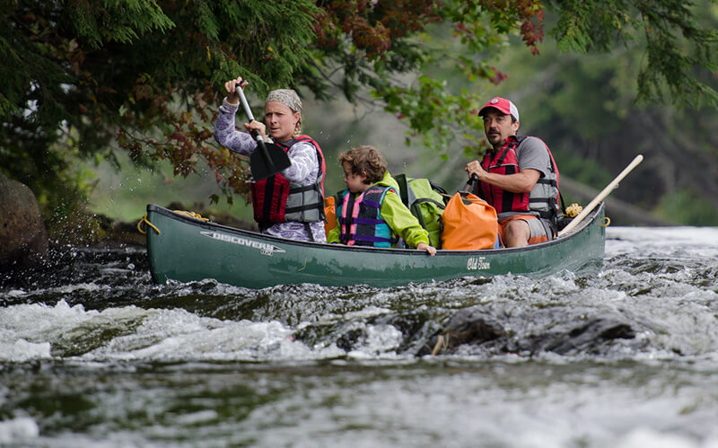 Two paddlers with a child running a small rapid in a tandem green Old Town canoe