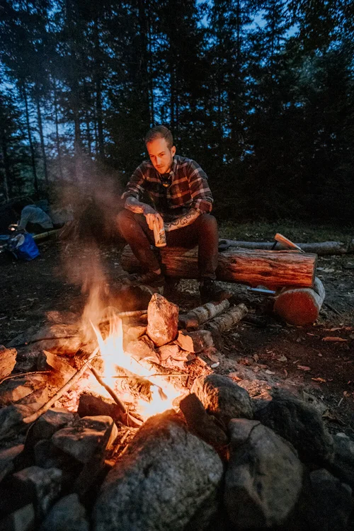 A man sits by a campfire at night. 