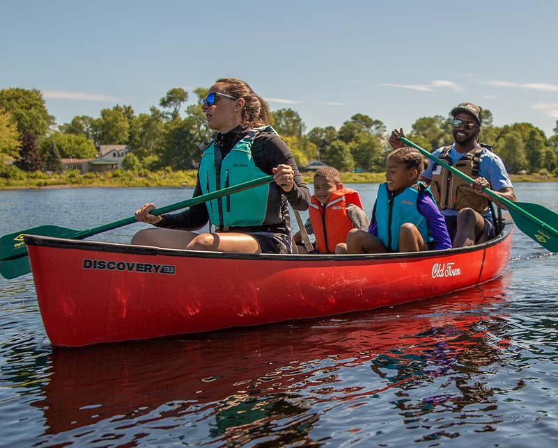 Family wearing various Old Town Life Jackets paddling in the Old Town Discovery canoe