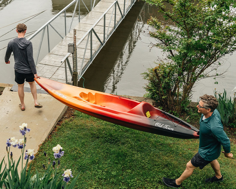 Two men using carrying handles to transport the Old Town Twister kayak