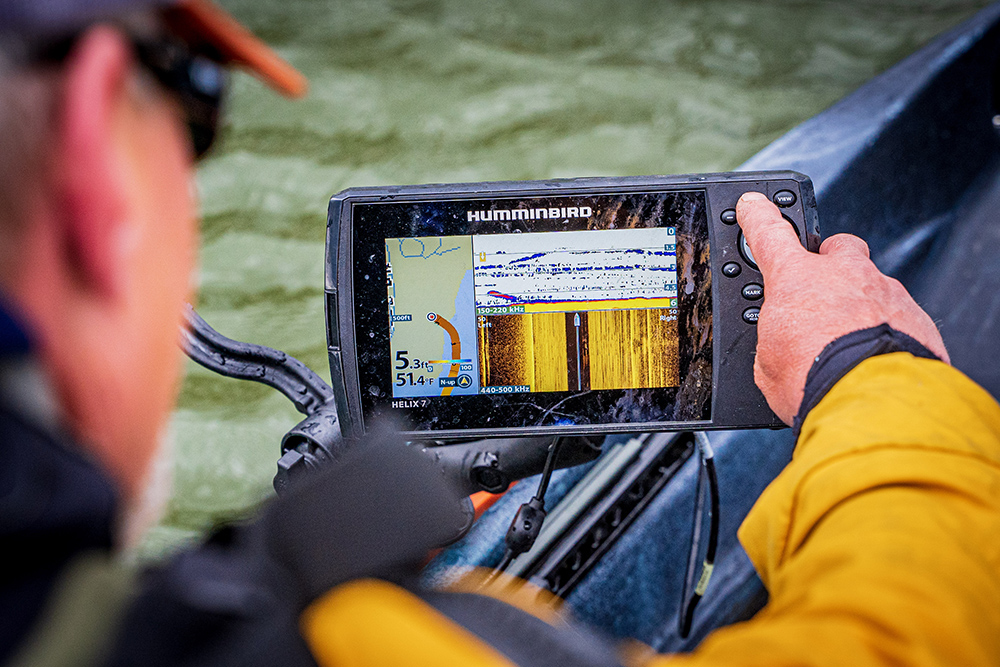 A male kayak angler pushes a button on his Humminbird HELIX fish finder on a fishing kayak.