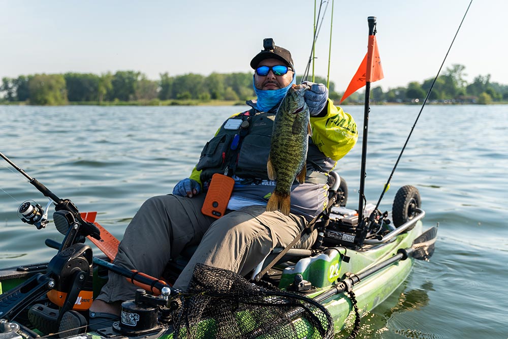 Man in Old Town Predator fishing kayak holding up large caught fish
