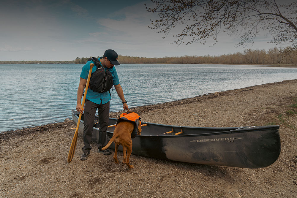 Man with dog on shore with Old town Discovery canoe