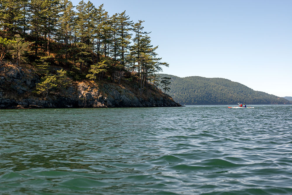 Two Old Town touring kayaks paddling in distance towards beautiful mass of wooded land