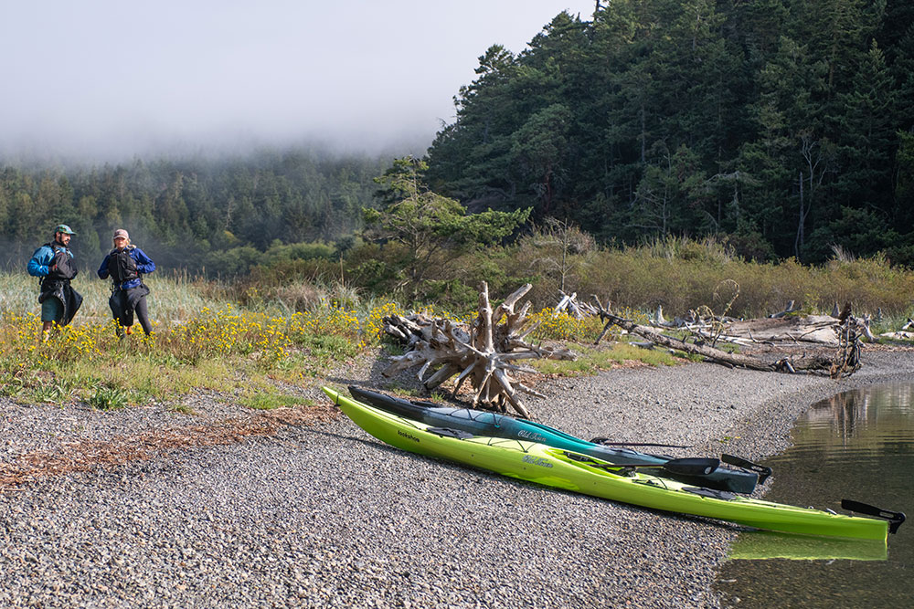 Man and woman with hands in lifejackets standing near shore with two Old Town touring kayaks