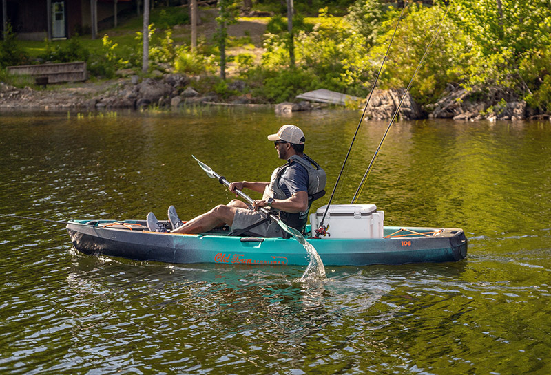 A man paddles a teal sit on top fishing kayak on a calm but muddy lake.