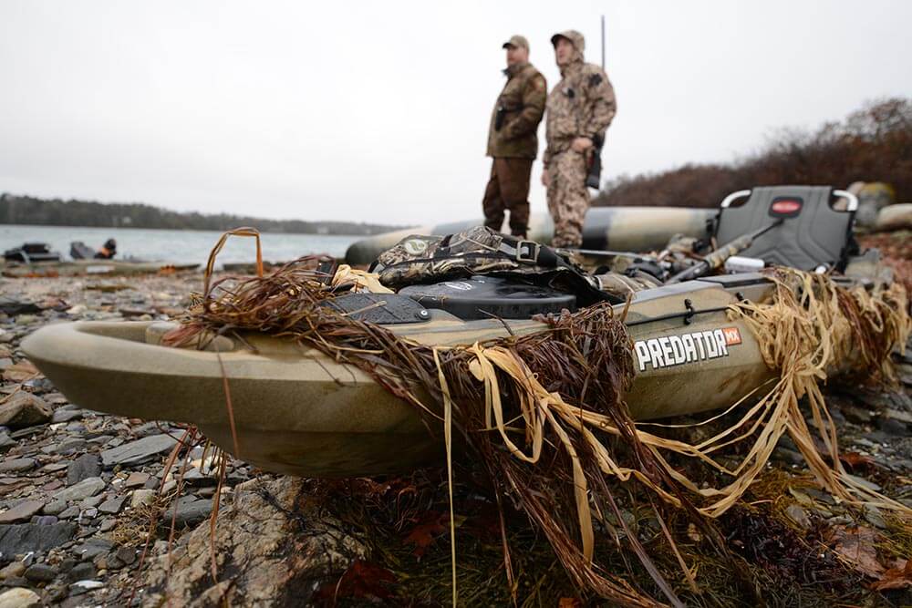 Two men in hunting gear standing next to camouflaged Old Town Predator MX hunting kayak