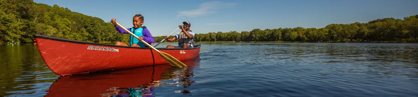 Father and daughter paddle a red Saranac canoe on a river