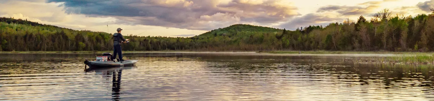 Kayak angler stand up casting at sunset on a mountain lake