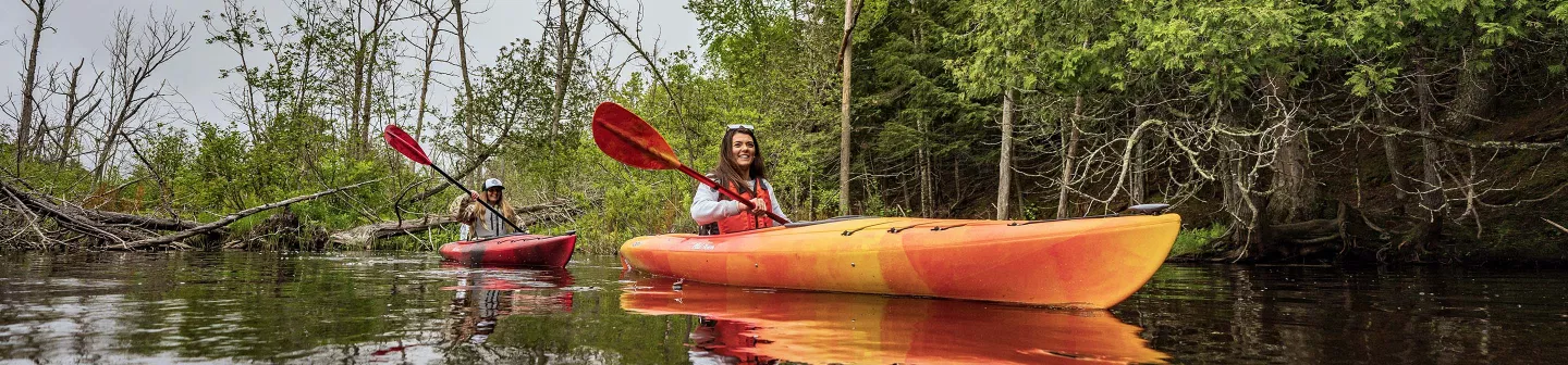 Two women paddle Old Town loon kayaks on a calm small river.