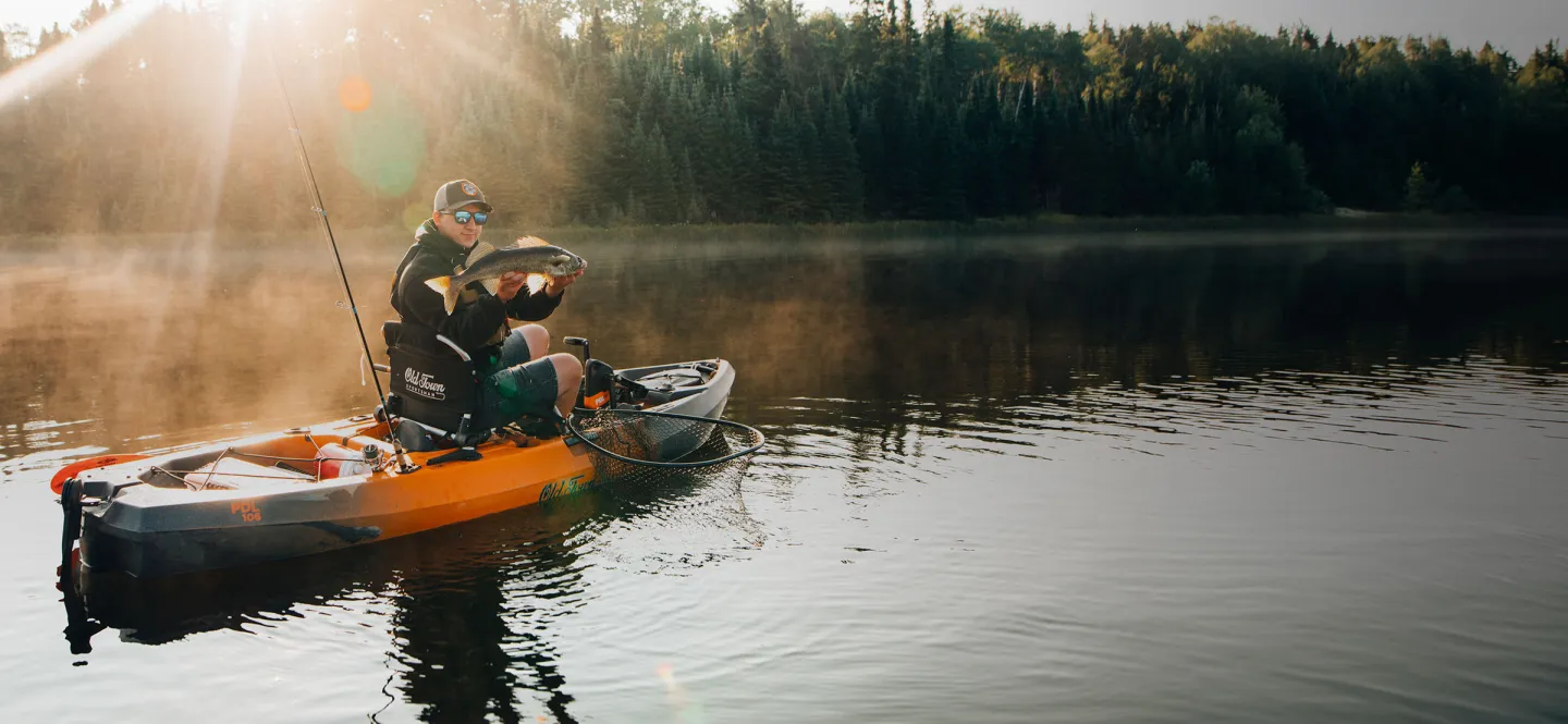 Man holding up caught fish on the Old Town Sportsman PDL 106 fishing kayak with sunsetting in background 