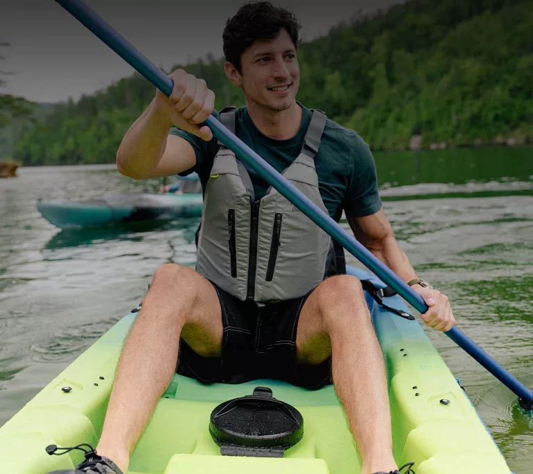 A young man paddles a yellow sit on top kayak. 