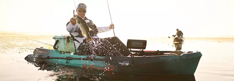 Man holding up a caught fish while in the Old Town Sportsman 106 Powered by Minn Kota kayak