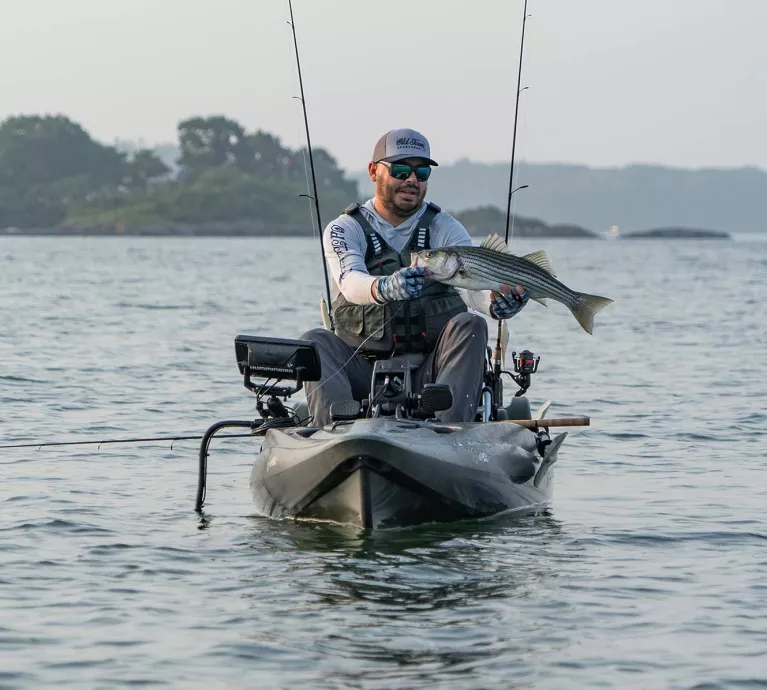 Man holding a caught fish while in the Old Town Sportsman BigWater PDL 132 fishing kayak