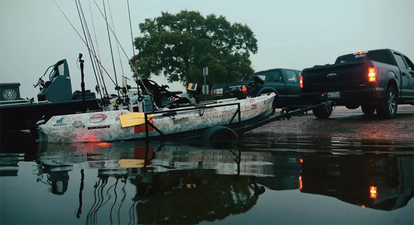 A truck backing a kayak down a boat ramp.