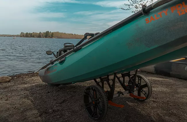 An Old Town fishing kayak sitting on a kayak cart next to a calm lake.