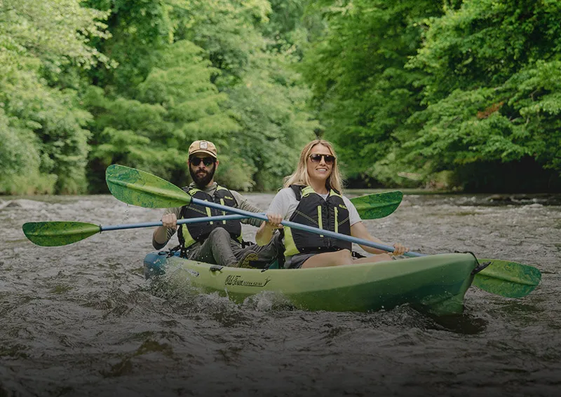 Two kayakers paddle a tandem kayak down a river. 